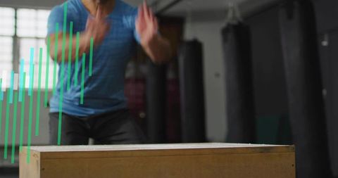 Male athlete performing explosive plyo box jump in gym with punching bags and motion blur