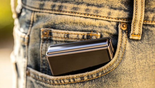 Foldable clamshell smartphone peeking from denim pocket with sunlight reflection, closeup tech