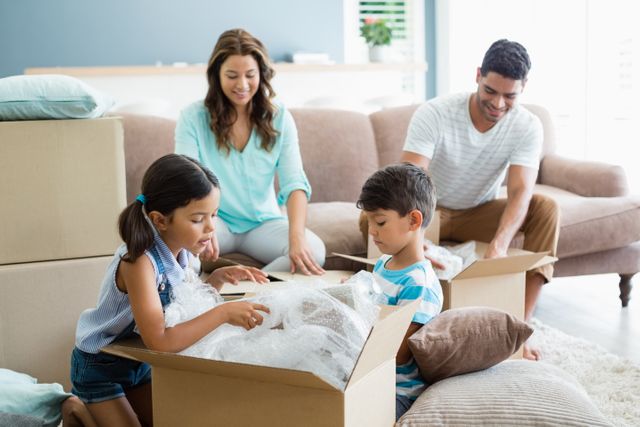 Parents and kids unpacking carton boxes in living room at new home