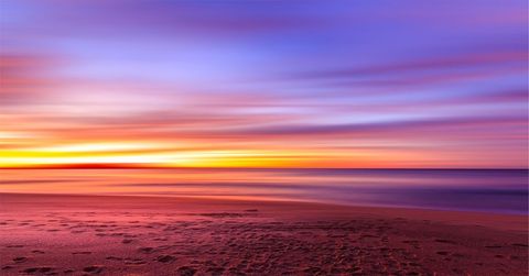 Long-exposure sunset glowing over tranquil beach with colorful sky and footprints