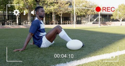 Male athlete sitting on turf with white oval ball and rec overlay, campus training moment