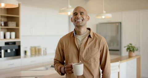 Smiling man holding coffee mug in bright modern kitchen with island and pendant lights