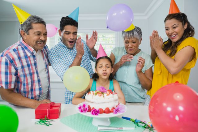 Multigenerational family celebrating a child's birthday at home. Grandparents, parents, and child gathered around a birthday cake with balloons and decorations. Perfect for themes of family bonding, celebrations, and joyful moments. Ideal for use in advertisements, greeting cards, and articles about family events and traditions.