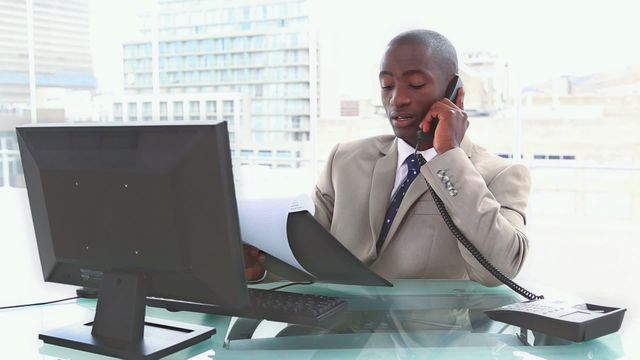 A businessman in a suit is seated at an office desk, engrossed in a phone conversation while holding a file. With a view of city buildings through the office window backdrop, the image conveys themes of professional communication and diligence. Ideal for business websites, corporate articles, or office-related promotions to illustrate workplace scenarios.