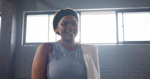 Smiling woman cooling down after workout with towel and headband in industrial gym