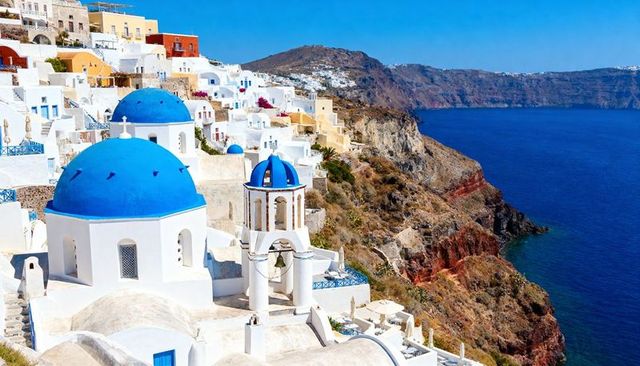 Cascading santorini village clinging to caldera with blue domes and aegean sea panorama