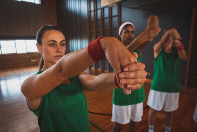 Diverse female basketball team stretching hands in gym. Ideal for content on sports training, teamwork, fitness routines, and promoting healthy lifestyles. Suitable for articles, blogs, and advertisements related to women's sports, athletic training, and team-building activities.