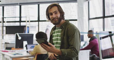 Man holding tablet in collaborative open-plan workspace projecting code on glass wall