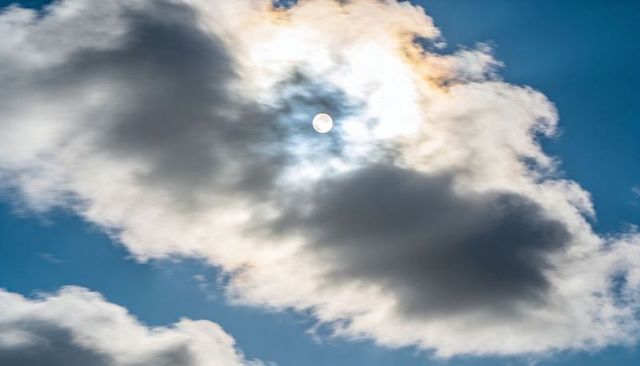 Iridescent cumulus revealing sun disc in bright blue sky with glowing halo and contrast