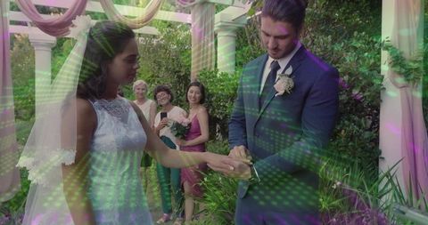 Groom placing ring on bride under pergola during outdoor garden wedding ceremony