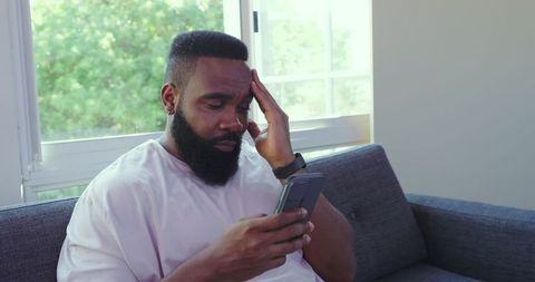 Pensive man holding smartphone at home near window