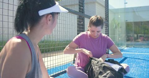 Midlife woman packing duffel bag after outdoor padel practice on bright blue turf court