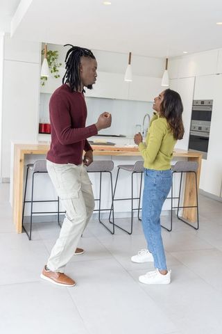 Young interracial couple dancing and chatting in modern bright minimalist kitchen