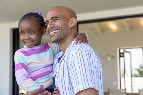 African american father carrying smiling daughter, hugging and enjoying family moment home