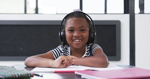 Smiling girl with headphones studying in classroom