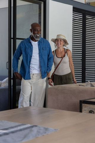 Mature couple entering modern living space smiling and relaxed with sun hat and denim
