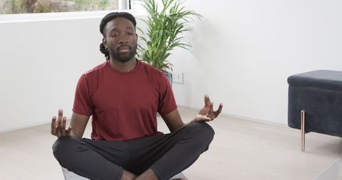 African American Man Meditating Cross-Legged at Home with Houseplant and Minimal Interior