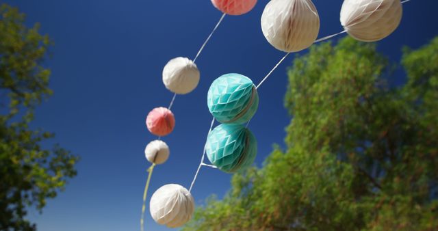 Colorful paper lanterns are strung against a clear blue sky, with copy space. These festive decorations add a playful and cheerful atmosphere to outdoor events or celebrations.
