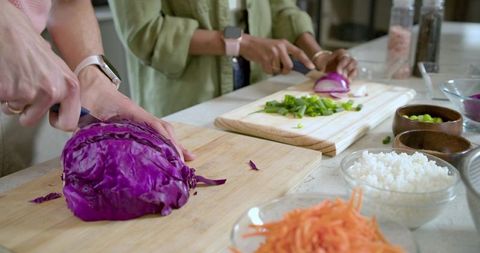 Diverse pair chopping purple cabbage and slicing red onion on countertop preparing vibrant bowls