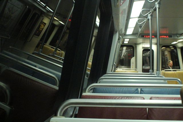 This image depicts the interior of an empty metro train with only one visible passenger in the distance. The clean seats and modern design are evident, highlighting the sleek interior common in urban public transportation. This could be used for themes related to public transit, urban commuting, or infrastructure.