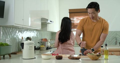 Asian couple cooking in modern kitchen man crushing spices with mortar and pestle