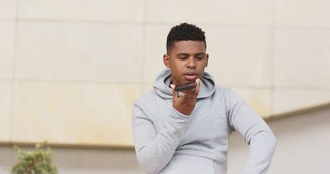 African american man speaking into smartphone outdoors wearing light gray hoodie