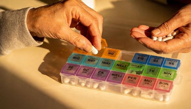 Senior hands sorting weekly pill organizer on sunlit kitchen table with white tablets