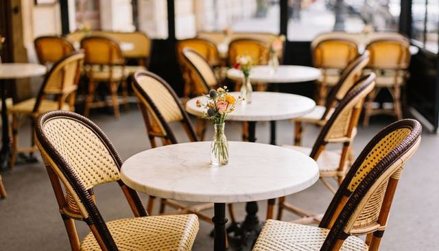 Cozy bistro tables with marble tops and rattan chairs featuring fresh floral vases
