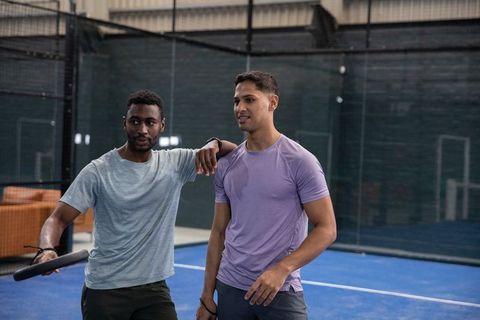 Two male athletes resting on blue padel court after training session