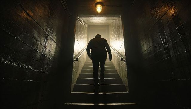 Silhouette man climbing dim concrete stairwell toward bright exit
