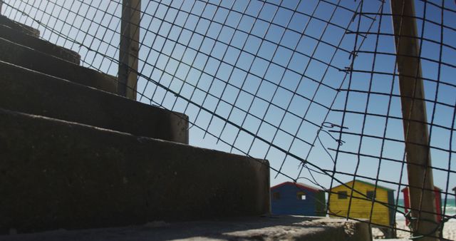 View through partial fencing on multicolored beach huts near stairs - Download Free Stock Images Pikwizard.com