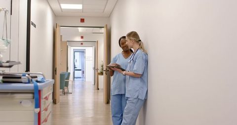 Two nurses consulting tablet in modern hospital corridor, clinical collaboration and care