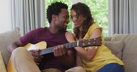 Biracial Couple Bonding Over Guitar at Home on Sofa