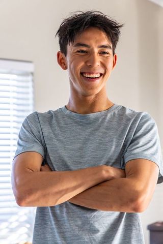 Smiling young asian man standing with arms crossed wearing light gray tee and stud earring