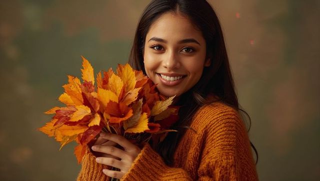 Cheerful woman wearing cozy sweater holding autumn leaves bouquet