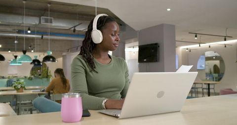 African american woman working on laptop with headphones in modern coworking space for productivity