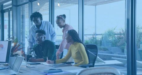Collaborating team brainstorming around laptop and analytics chart in modern glass office