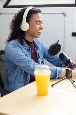 Non-binary podcaster recording in studio wearing denim jacket and white headphones