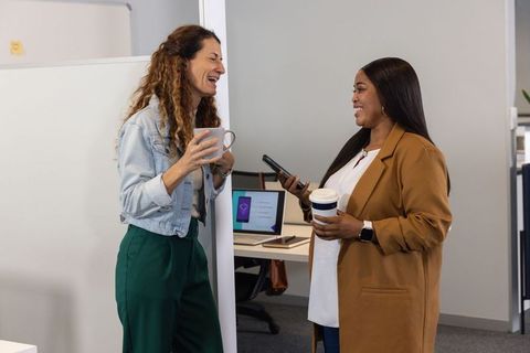 Diverse female coworkers chatting over coffee in modern office business collaboration