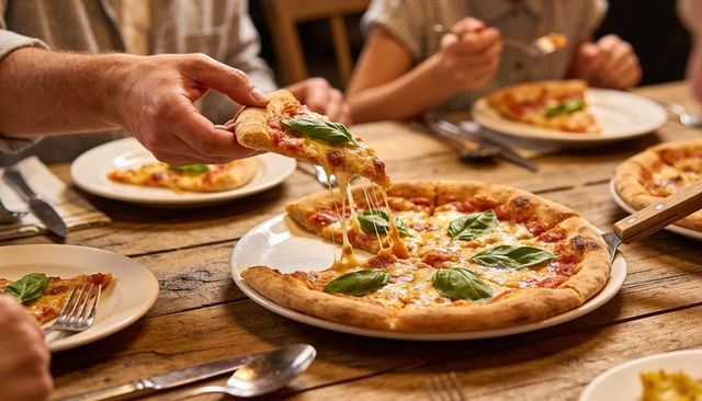 Pulling melty margherita pizza slice with fresh basil on wooden table, cozy dinner