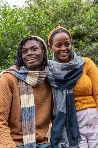 Young couple posing outdoors wearing knit scarves and mustard sweaters smiling warmly