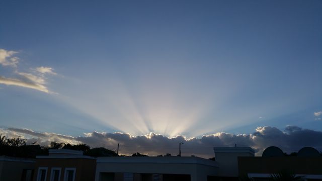 Sun rays breaking through clouds over an urban rooftop skyline. Perfect for use in projects related to weather, city living, peaceful evenings, and sunset scenes. Could be used in websites, marketing materials, inspirational posters, or background imagery for presentations.