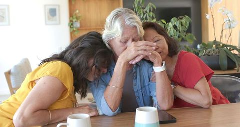 Senior woman receiving comfort from adult friends during emotional moment at home