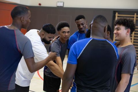 High school boys basketball team huddle with coach building unity, leadership and focus