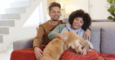 Young couple cuddling with golden retriever on cozy modern living room sofa at home