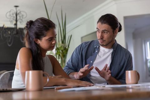 Young couple discussing finances and budget planning at home dining table with coffee mugs