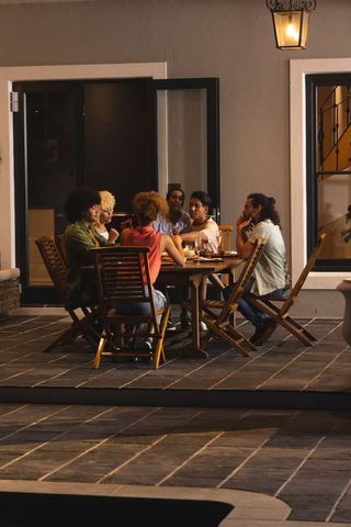 Evening terrace dinner party with diverse friends sharing meal on wooden patio table