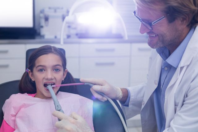 Dentist examining young girl with dental tools in modern clinic. Ideal for illustrating pediatric dentistry, dental care for children, healthcare services, and oral health education. Can be used in medical articles, dental clinic websites, and promotional materials for dental practices.
