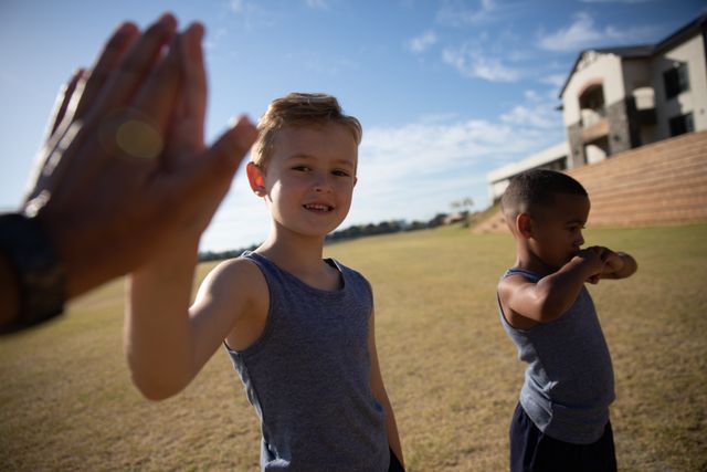 Two elementary schoolboys are high-fiving on a soccer field, showcasing teamwork and friendship. This image is perfect for promoting childhood sports programs, outdoor activities, and educational content related to physical education. It can also be used in advertisements for summer camps, youth sports leagues, and community events.