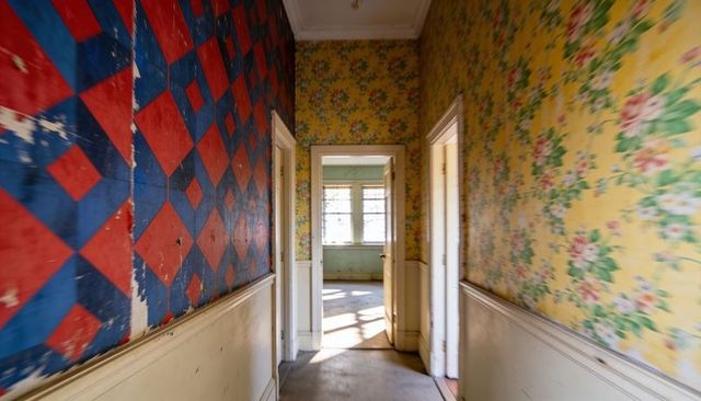 Sunlit vintage hallway with peeling red-blue diamond wallpaper and floral yellow walls